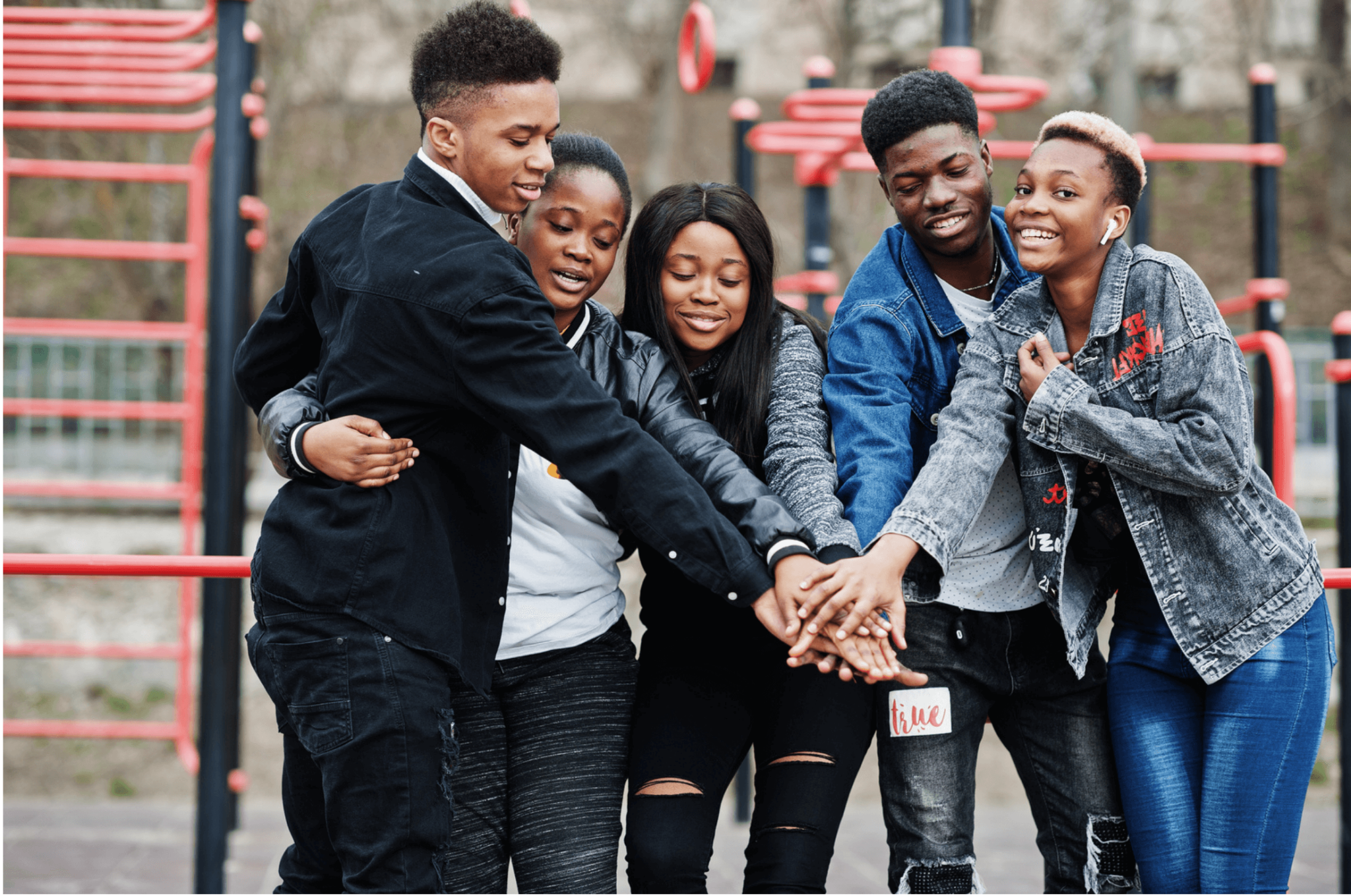 5 teens put their hand in as a team on a playground