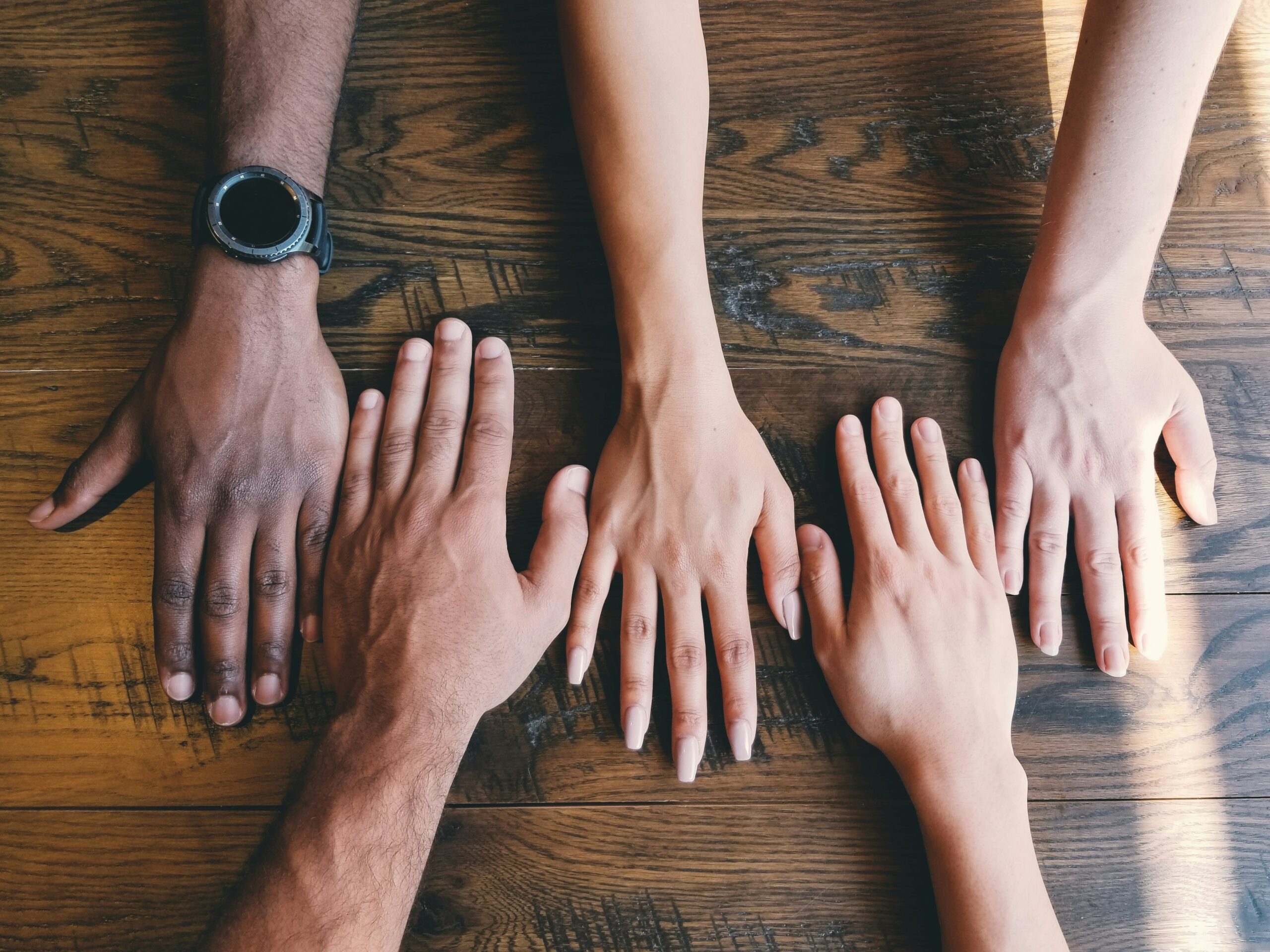 5 diverse willing hands aligned on a wooden table