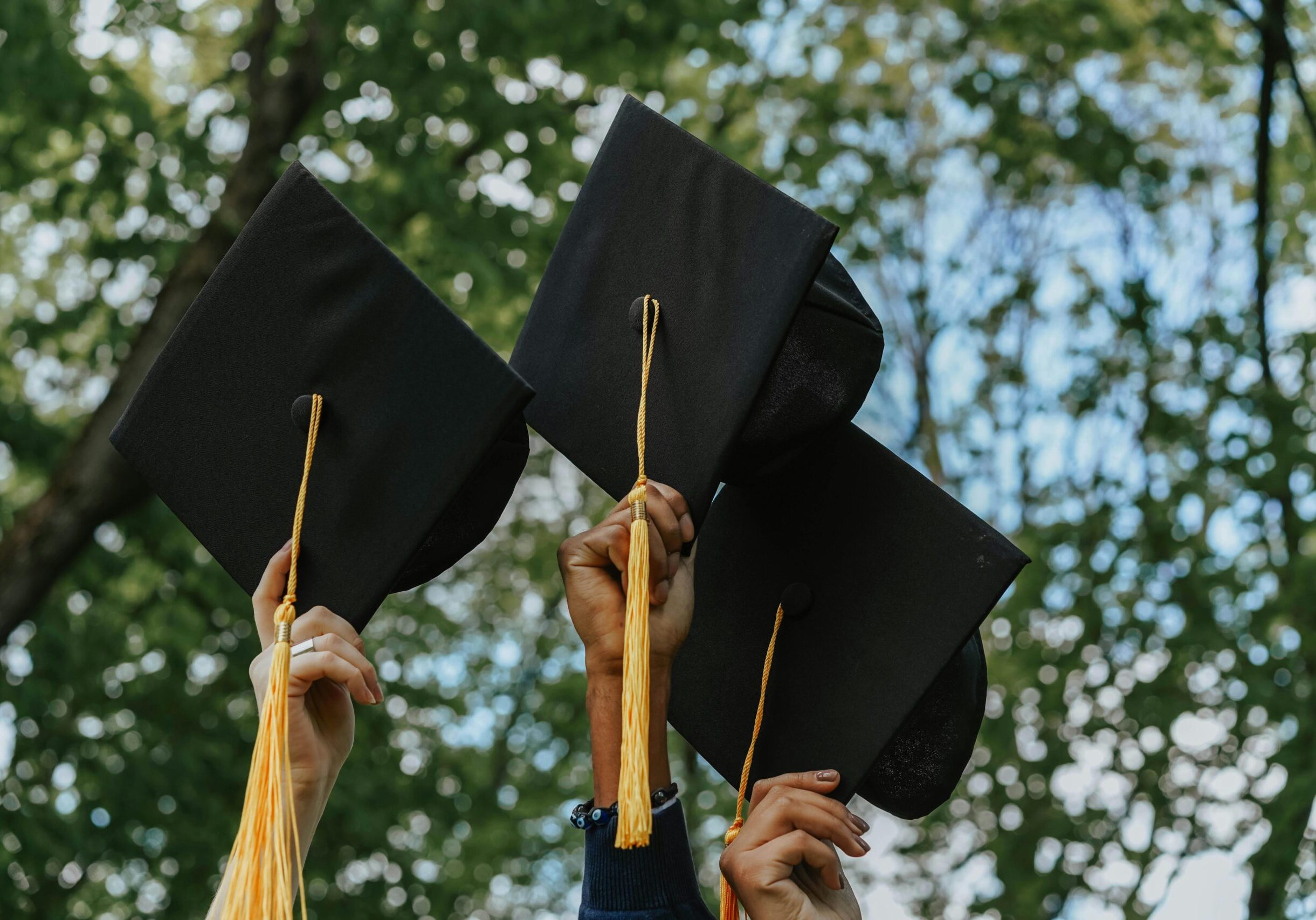 Three hands raising black and gold graduation caps in the air