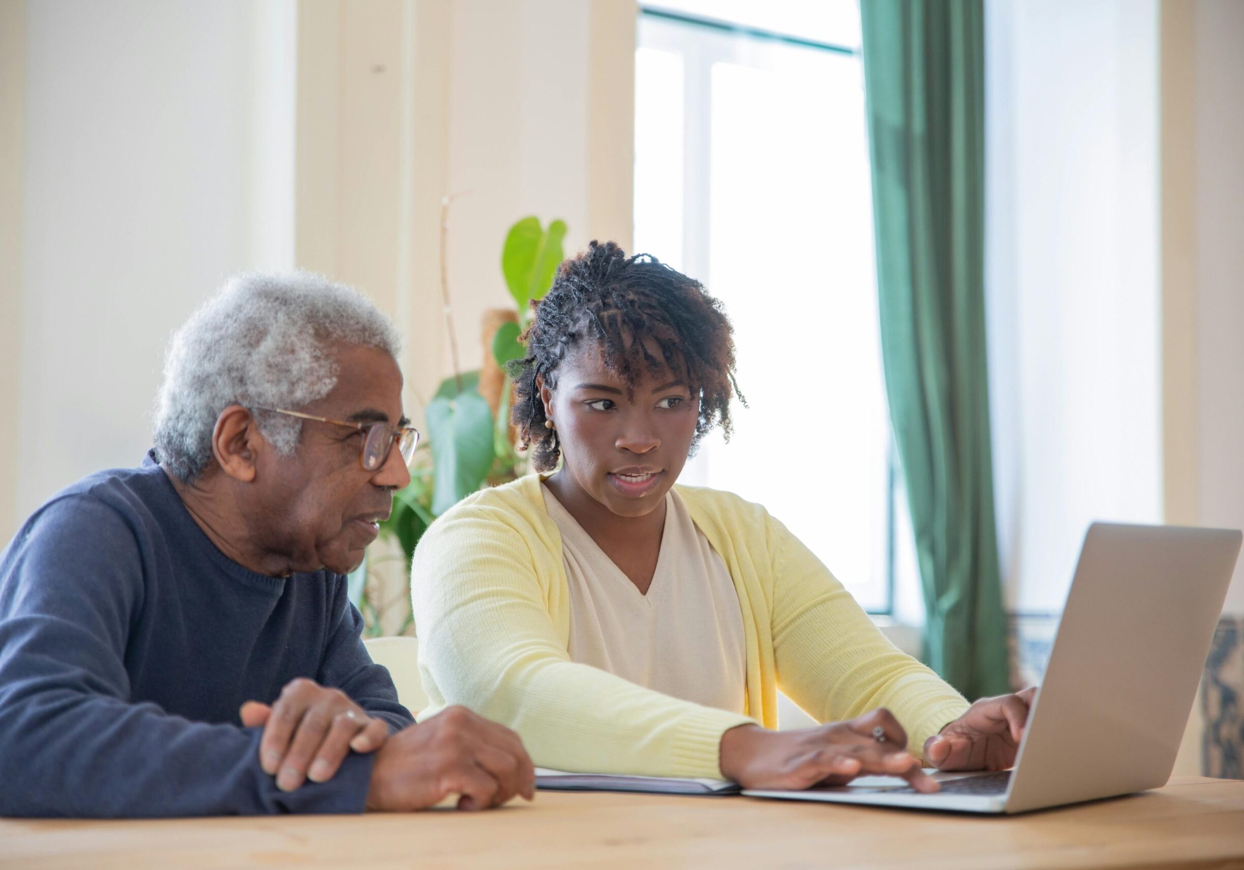 A middle-aged woman is sharing a laptop screen with an elderly man.