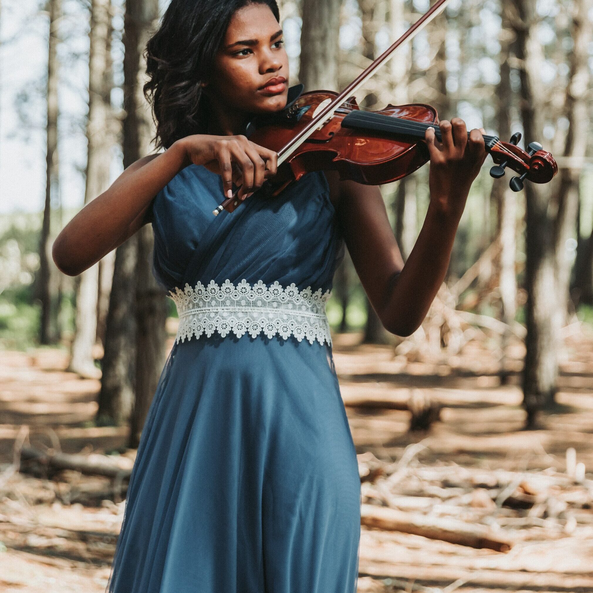 young woman in dress playing violin in the woods